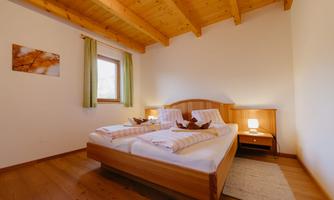 A cozy bedroom with a wooden bed and two pillows. Bright walls and windows with curtains create a pleasant atmosphere.
