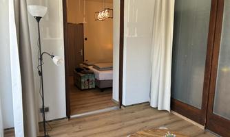 A modern room with a wooden floor and a large window. The walls are decorated with white curtains and a warm wood design.