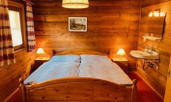 A cozy bedroom with wooden walls and a large bed.  
On the nightstand, there are two lamps and there is a sink in the corner.