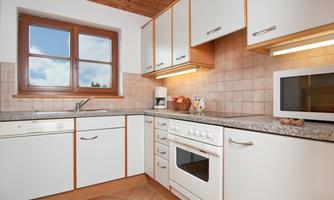 A modern kitchen with white cabinets and a granite countertop. Windows provide plenty of light and a pleasant atmosphere.