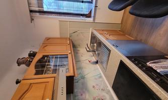 A modern kitchen with wooden cabinets and a stove. The room is bright and well-equipped, with a window that lets in light.