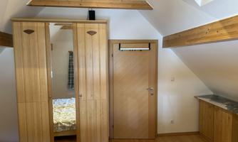 A cozy room with wooden shelves and a large wardrobe. The walls are light and the floor is made of wood.