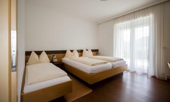 A cozy room with three beds and beige bedding. Large windows ensure plenty of daylight.