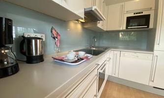 A modern kitchen with white cabinets and a bright countertop. On the countertop, there is a coffee machine, cups, and a small floral decoration.