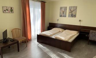 A cozy room with a double bed and two pillows. Next to the bed are a table, a chair, and a television.