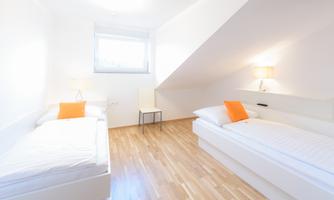 A bright bedroom with two single beds. The furniture is modern and the walls are in neutral colors.