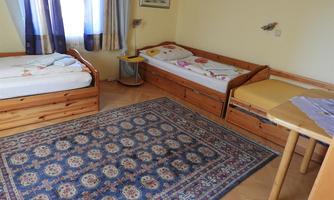 A cozy room with two single beds and a large carpet. There is a table and a window with curtains.