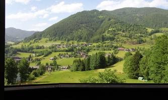 A picturesque view of green hills and dense forests. In the foreground, some houses and a part of a small village are visible.