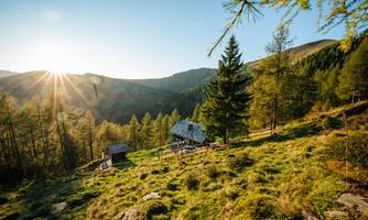 A picturesque mountain landscape with a small cottage and trees. The sun is shining and gives the scene a warm atmosphere.