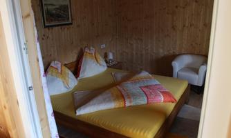 A cozy bedroom with a large bed and colorful bedspreads. The walls are made of wood, and there is a comfortable armchair in the corner.