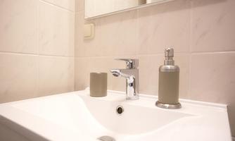 A modern sink with a shiny faucet. On the shelf are two decorative containers in neutral tones.