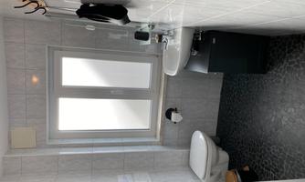A small, modern bathroom with white tiles and a window. There is a toilet, a sink, and a towel holder.