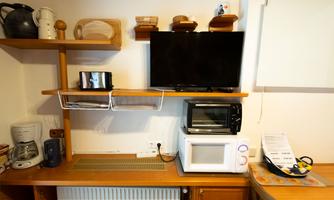 A small kitchen corner with a television, microwave, and toaster. Various kitchen utensils and appliances are visible on the shelves.