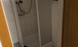 A small shower with white tiles and a gray floor. A towel hangs outside the door.