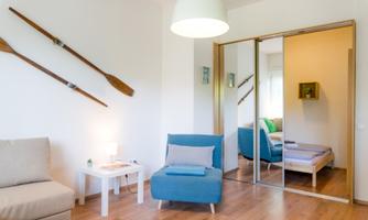A modern living room with a blue armchair and a cozy couch.  
Rowing oars are hanging on the wall, and a large mirror reflects the space.