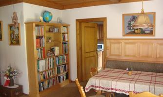 A cozy room with a bookshelf and a dining table. The walls are decorated with pictures and decorative elements.