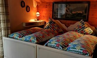 A cozy bedroom with two beds and colorful bedspreads. The walls are made of wood, and there is soft lighting.