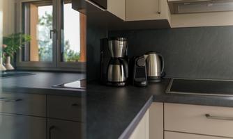 A modern kitchen with a dark workspace. There is a coffee machine and a kettle on the countertop.