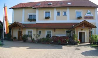 A cozy guest house with a red roof and blooming plants at the entrance. The facade is designed to be friendly and inviting.