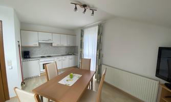 A bright and modern kitchen with a dining table and chairs. Large windows provide plenty of natural light.
