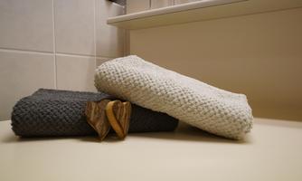 A gray and a white towel lie together on a light surface. Two wooden hearts are placed in between.