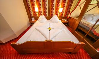 A cozy bedroom with a large double bed and decorative pillows. The walls are designed with a beautiful pattern in warm colors.