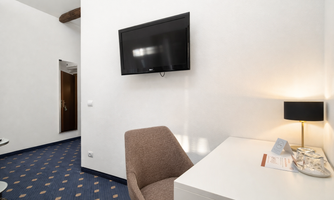 A modern room with a TV on the wall and a desk. A comfortable chair and a desk lamp are visible.