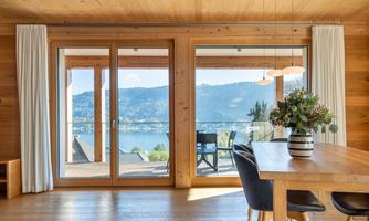A bright, modern living room with large windows and a view of a lake. The table is elegantly set, and a plant decorates the center.