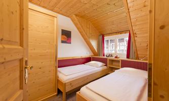 A cozy room with wooden paneling and two single beds. The window offers a view of a peaceful surroundings.
