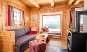 A cozy room with wooden walls and a large windowsill. There is a sofa, a small table, and a stove that creates a cozy atmosphere.