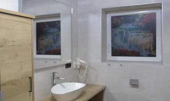 A modern bathroom with a wooden cabinet and a stylish sink. The large window offers a beautiful view of a waterfall.