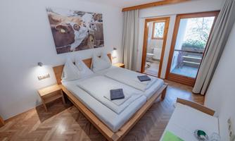 A cozy room with two single beds and a wood design. In the background, there is a balcony with a view and a cow painting on the wall.