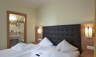 A cozy bedroom with a large double bed and modern lights. In the background, the bathroom is visible.