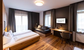 A modern hotel room with a cozy bed and a seating area. Large windows provide plenty of daylight and an inviting atmosphere.