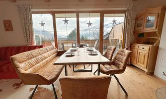 A cozy dining area with a table and modern chairs. Large windows offer a view of the mountains and let in plenty of light.