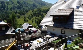 A picturesque mountain village with traditional houses and a playground. The surroundings are enclosed by green hills and mountains.