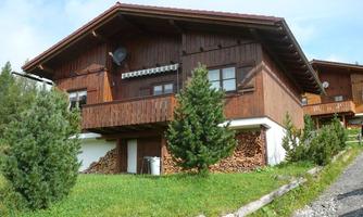 A traditional chalet-style wooden house in a green environment. In front of the house, a pile of wood is stored.