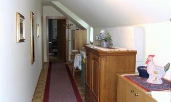 A narrow hallway with wooden flooring and a red carpet. Pictures are hanging on the wall, and decorative items are on a sideboard.