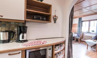 A modern kitchen with cooking appliances, including a coffee machine and microwave. A cozy living area is visible behind the arch.