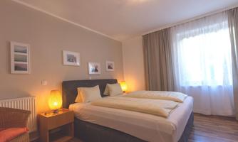 A cozy bedroom with a double bed, soft lighting, and bright curtains. Pictures hanging on the walls give the room a personal touch.