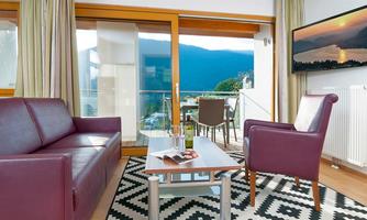 A stylish living room with a purple sofa and an armchair. Large windows offer a beautiful view of the landscape.