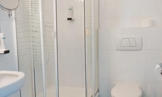 A modern bathroom with a glass shower, sink, and toilet. The floor is tiled with green tiles.