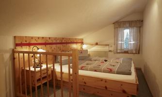 A cozy bedroom in the attic with wooden paneling. It features a double bed, nightstands, and a window that lets in daylight.