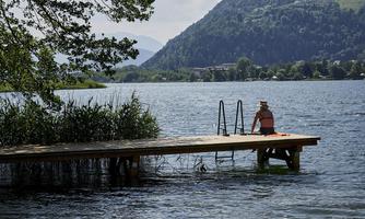A quiet dock by the water with a person gazing at the lake. In the background, gentle hills and lush greenery can be seen.