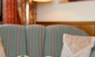 Three green apples on a glass plate are on a table. Next to them lies a key and a round coaster.