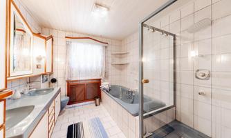 A bright bathroom with a shower and a bathtub. There are sinks and large windows for plenty of light.