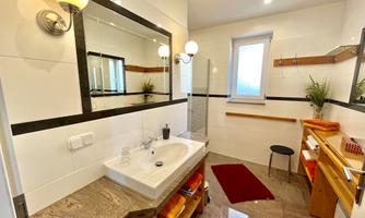 A modern bathroom with a sink, mirror, and wooden shelves. The walls are painted in light colors and there is a large mirror above the sink.