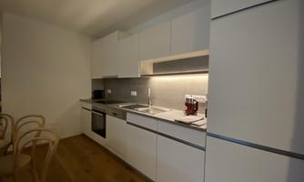 A modern kitchen with white furniture and an elegant countertop. There is a stove, a sink, and space for a dining table.