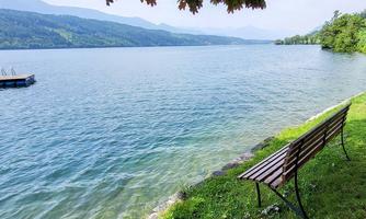 A quiet lake with clear water and gentle hills in the background. A bench by the shore invites you to linger.