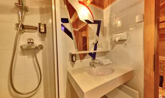 A modern bathroom with a shower and an elegant sink. The walls are brightly tiled, and there are wooden details in the ceiling area.